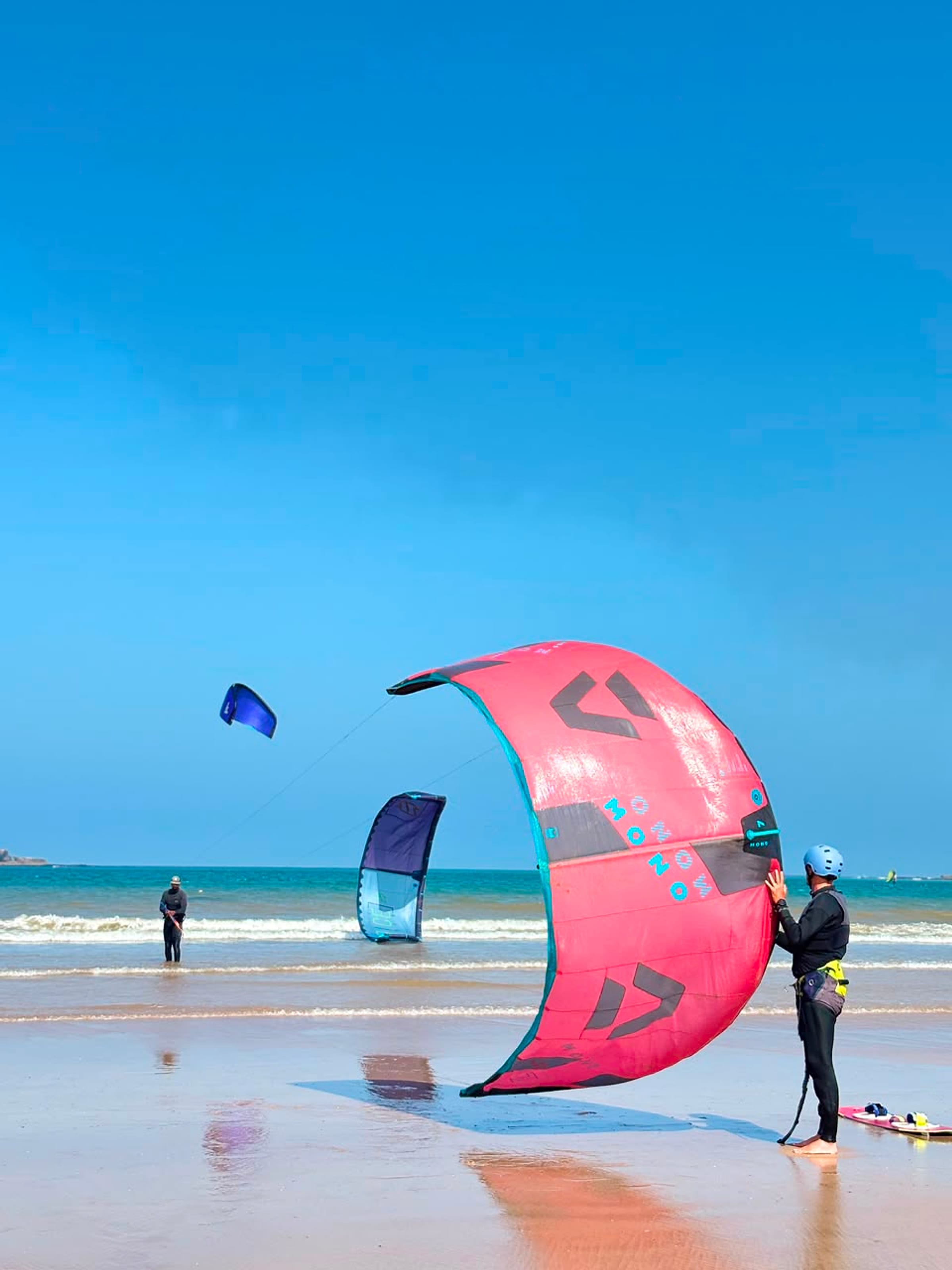 A pink kitesurf kite reflects on wet sand.