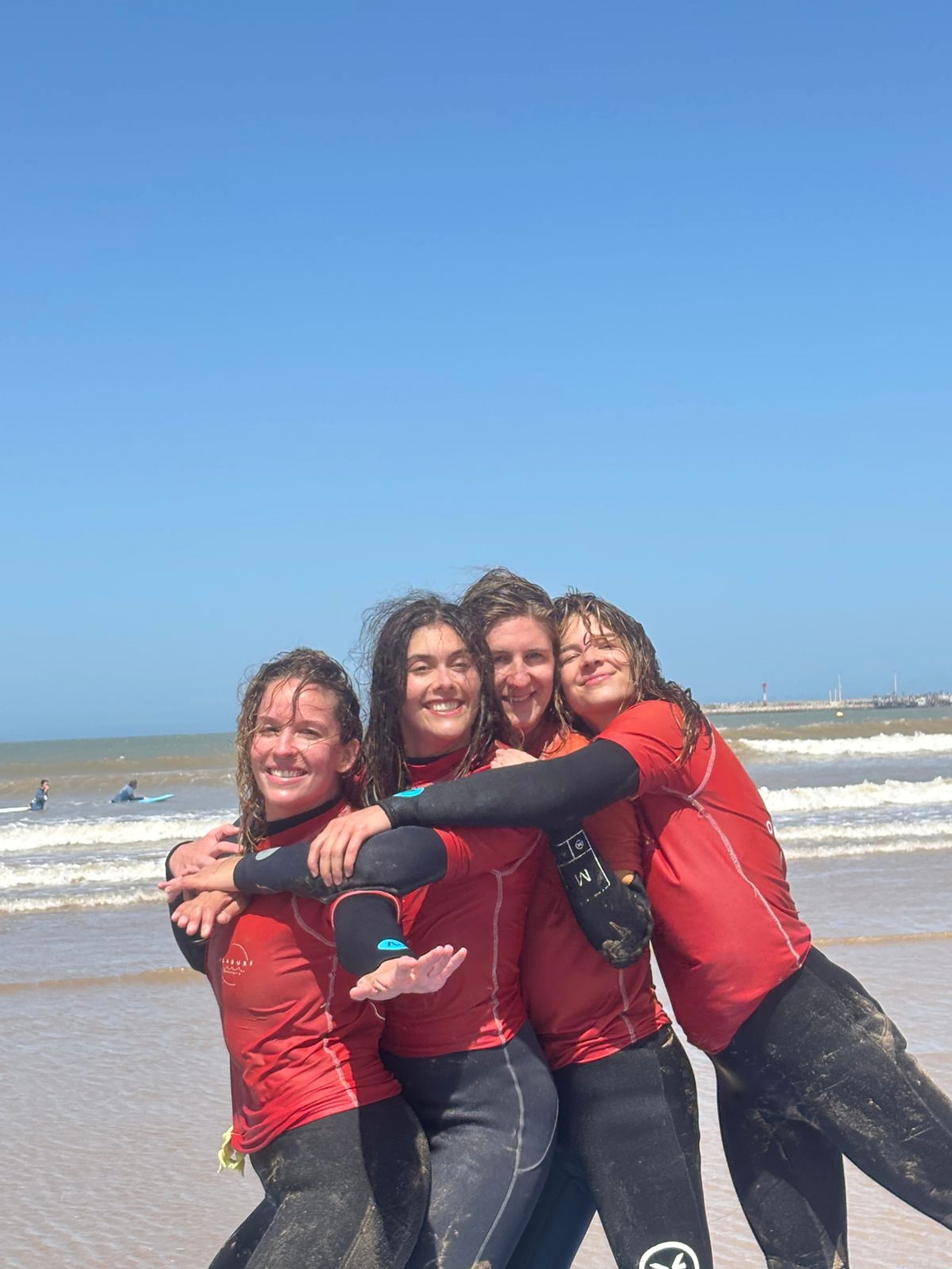 A group of friends stands with surfboards on Essaouira beach.
