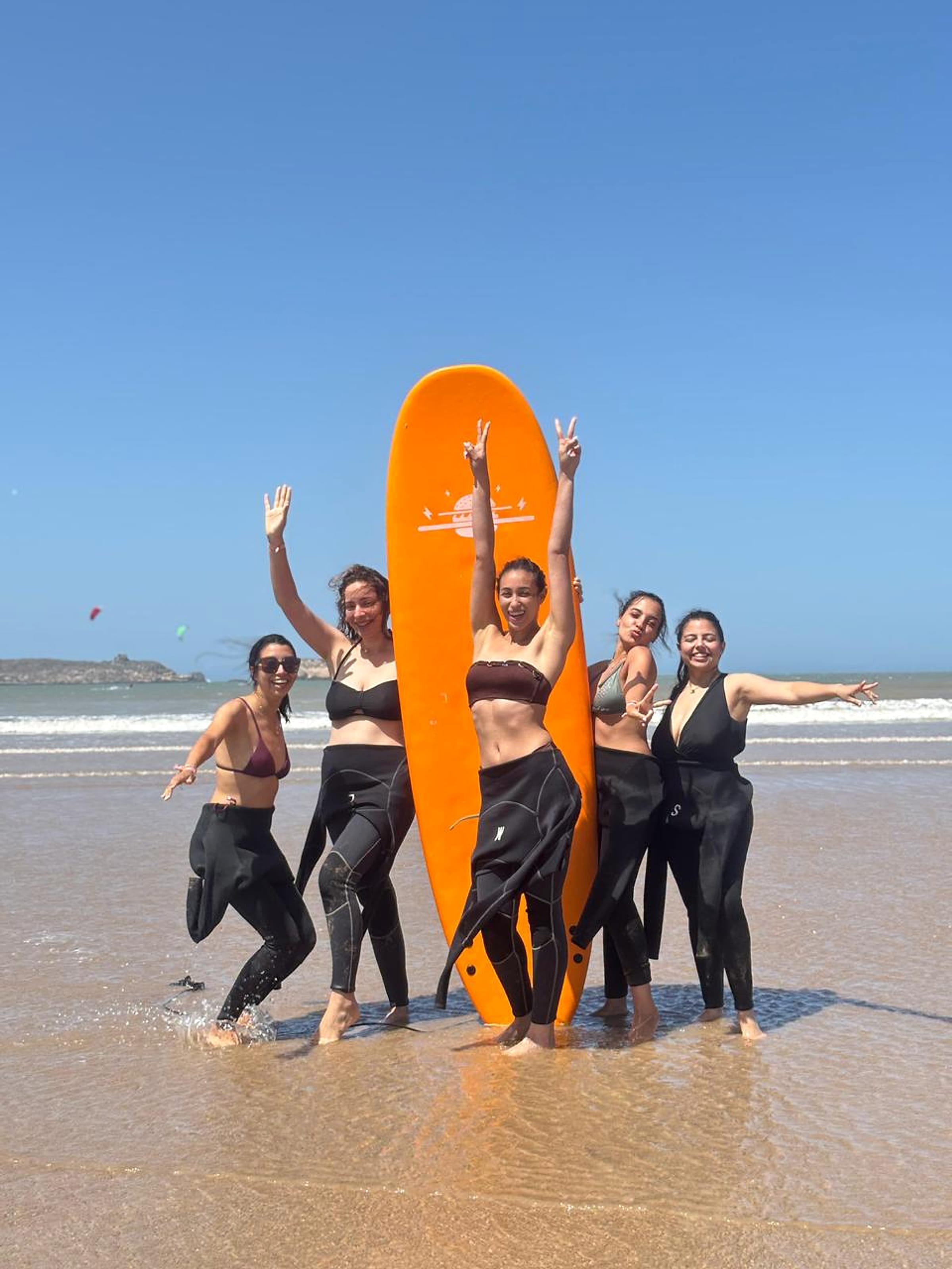 A surf group gathers around an orange board on the beach in Essaouira.