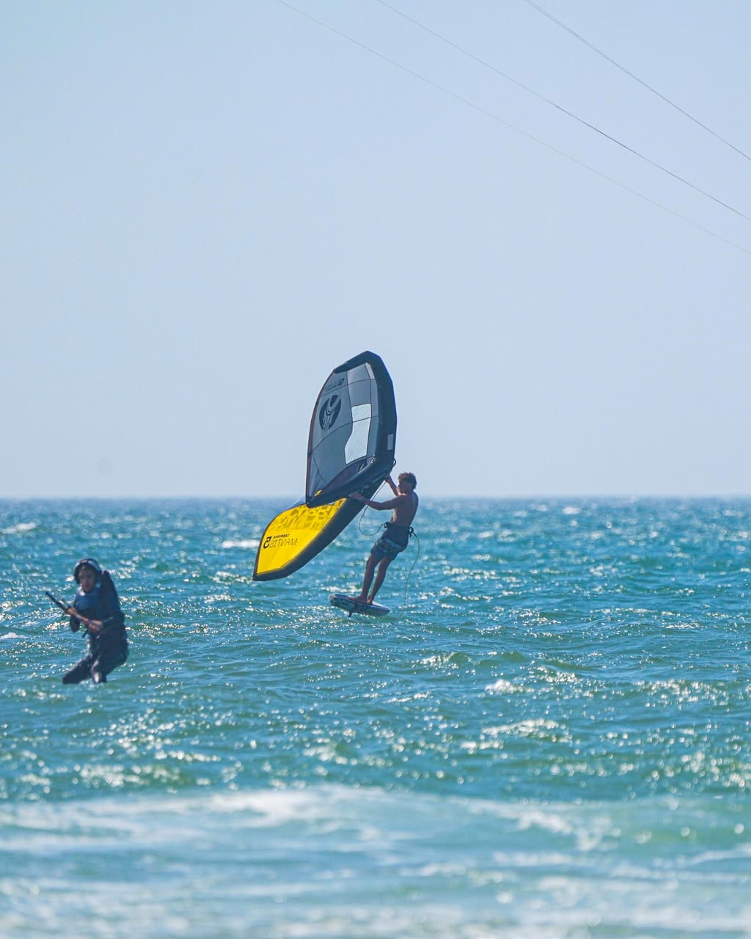 A wingfoil rider moves across textured water.